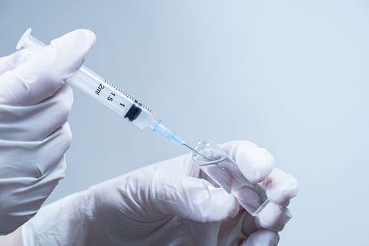 Hands in gloves preparing a medical injection shot. Concept of vaccination, providing medical service or taking a shot in clean laboratory or hospital conditions