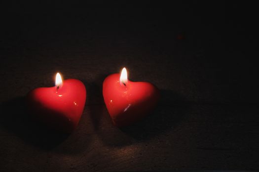 Two heart shaped candles burn in the darkness, copy space. Concept of the Saint Valentine's Day, love and romantics