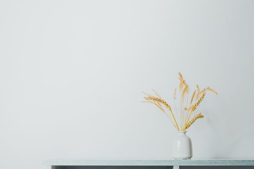 Spikelets or wheat in a vase on the table. Home decoration elements in sparse pastel background