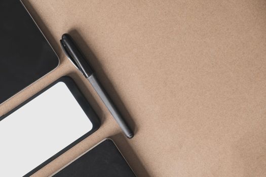 Business flat lay on brown paper background. Smartphone, tablet computer and notebook organizer on vintage background