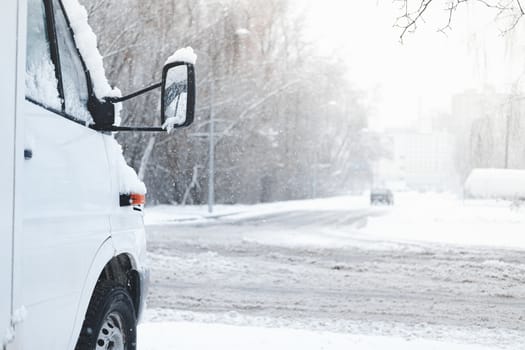 The front part of a car covered in snow. Vehicle stands by the snowy road in stormy weather