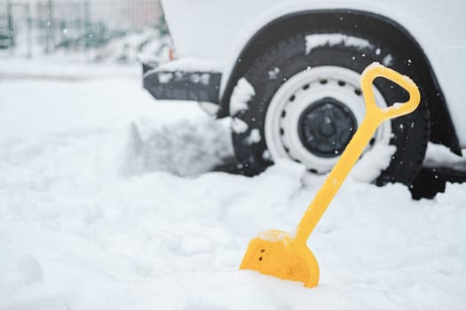 Car wheel in snow and a shovel. Concept of winter traffic problems, digging the vehicle out of the snow