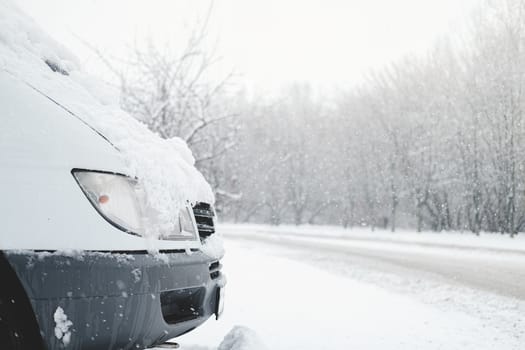 The front part of a car covered in snow. Vehicle stands by the snowy road in stormy weather