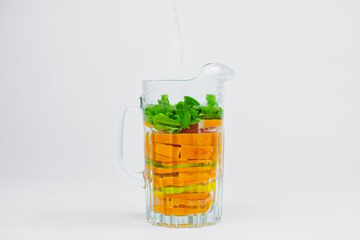 Large glass jar with citrus fruit and mint in white background. Preparing lemonade out of oranges, lime and lemons. Healthy and vitamins rich fruit drink