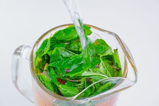 Pouring water over fresh peppermint leaves and grapefruit slices in a glass, close-up view. Preparing tonic water or lemonade, healthy fresh drink concept