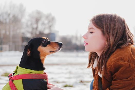 Portrait of a young woman and her lovely dachshund dog. Female and her pet at walk in the park, cold sunny day