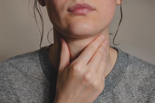 Sore throat, virus disease or flu. Woman holds hand against her throat feeling pain