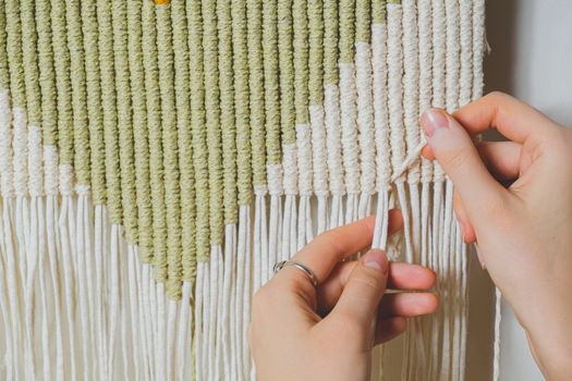 Hands doing macrame craft. Hand-making a cotton rope wall-hanging decor piece, concept of handicraft hobby or handworking