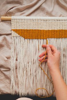 Handcrafted macrame wall hanging, close-up view. Human hand making a piece of decor