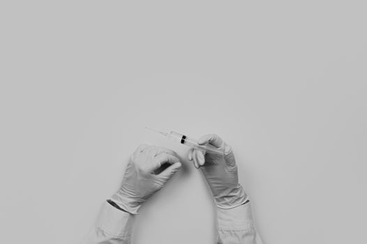 Medical doctor working place flat lay, faded monochrome. Top view of hands of MD holding syringe ready for injection on table with medical utensils