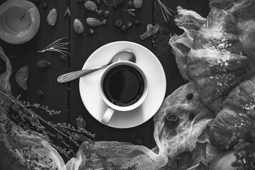 Cup of black coffee and croissants on dark monochrome background, top view. Flat lay of espresso and cornetto rolls on dark rustic table