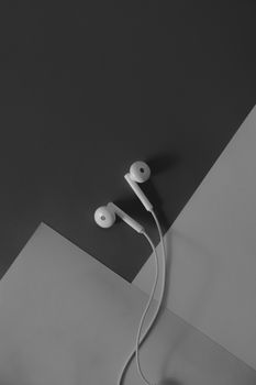pair of in-ear headphones on dark black and white background. Top view of a wired headset against dark grey backdrop