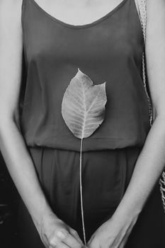 Woman in red dress holds an exotic green leaf, low key monochrome. Appreciating, loving nature concept: female with a beautiful leaf on her body