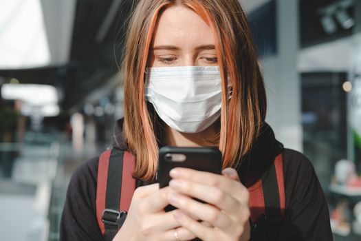 Woman in protective face mask using the phone at a public place. Coronavirus, COVID-19 spread prevention concept, responsible social behaviour of a citizen