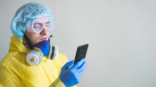 Medical worker in protective gear using smartphone after a shift. Concept of covid-19 epidemic, healthcare personell and overworking in hospitals. Doctor texting or chatting during break