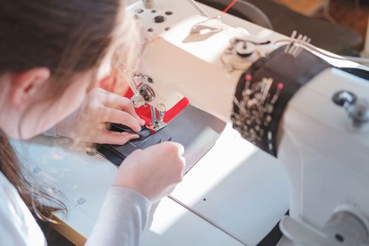 Seamstress doing precise work, shoulder view. Needlewoman at overlock sewing machine doing professional work, concept of labor