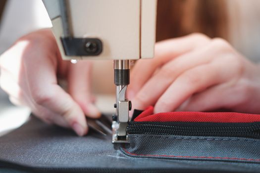 Hands of a seamstress doing precise work, close-up view. Needlewoman at overlock sewing machine doing professional work, concept of labor