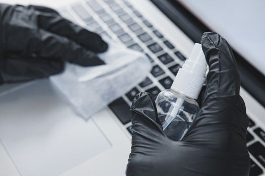 Cleaning laptop's keyboard with a sanitizer. Concept of hygiene and virus spread prevention at work or at home