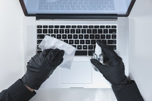 Cleaning laptop's keyboard with a sanitizer, top view. Concept of hygiene and virus spread prevention at work or at home