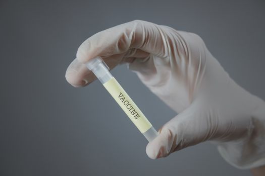 Hand in medical glove with a lab container - "vaccine" sign on it. vaccination, virus research or treatment development concept