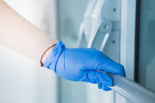 Hand in a rubber glove touches the handlebar of a door. Personal protection against germs, bacteria and virus: wearing hand gloves in public places