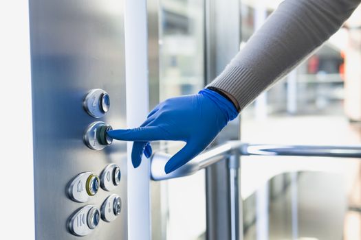 Hand in a rubber glove presses the elevator or lift button. Personal protection against germs, bacteria and virus: wearing hand gloves in public places