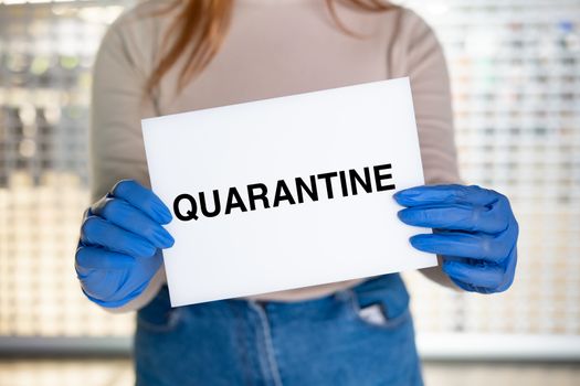 Quarantine sign in woman's hands. Female holds the sign plate against the closed store or shopping window