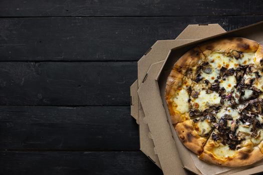 Pizza funghi in an open delivery box, dark backdrop. Delivery foods, takeaway food concept: pile of mushroom pizzas in boxes on black wood background