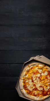 Pizza margherita in an open delivery box, dark backdrop with text space. Delivery foods, takeaway food concept: pile of pizza boxes on black wood background