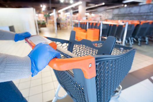 Hands in glives with a shopping cart at a supermarket. Grocery shopping, buying essential food at quarantine or covid-19 epidemic