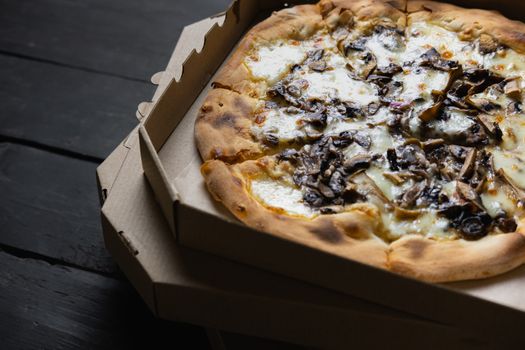 Pizza funghi in an open delivery box. Delivery foods, takeaway food concept: pile of mushroom pizzas in boxes on black wood background