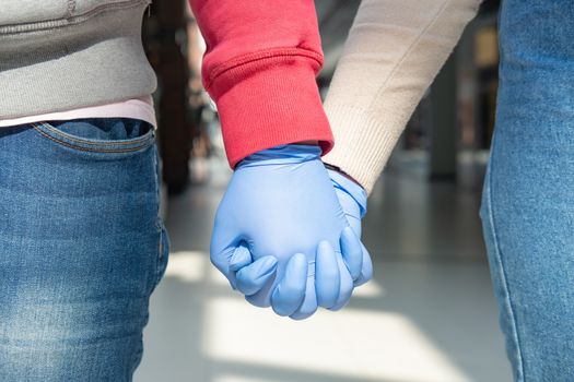 Two hands in rubber gloves holding each other. Concept of romantic relationship at quarantine, safe sex or protective measures