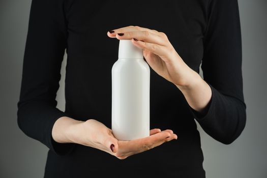 Generic white bottle in female hands against low light backdrop. Product photography, blank plastic bottle with space for brand text or logo