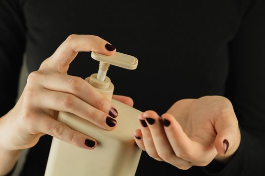 Bottle of hand sanitizer or soap in female hands, close-up view. Low-key image of personal hygiene, cleaning and self-care generic products