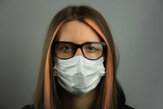 Intelligent woman in eyeglasses wearing medical mask. Young female in surgical mask in dark gray backdrop. Concept of personal hygiene, protection against virus and germs or professional gear