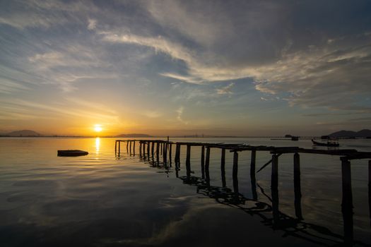 Landscape reflection of wooden bridge on sea in early morning at fisherman pier Jelutong, Penang. Penang Bridge at background.