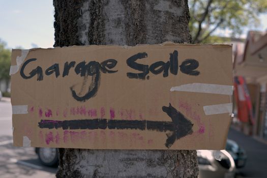 A hand made cardboard  sign for a garage sale taped to a tree