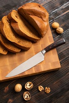 A loaf of bread sliced into slices with a knife on a wooden cutting board