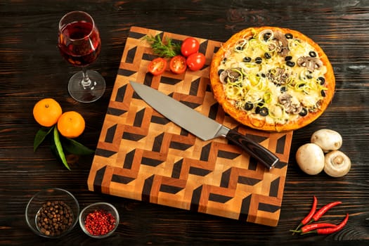 Pizza on a wooden cutting board next to vegetables, spices and a glass of wine