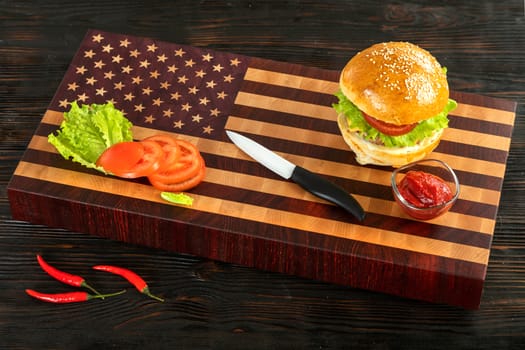 Burger next to vegetables and cheese on a wooden cutting board