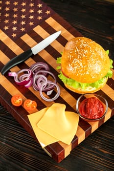 Burger next to vegetables and cheese on a wooden cutting board