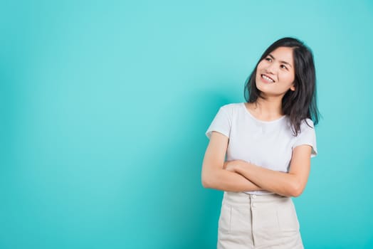 Portrait Asian beautiful happy young woman smile wear white t-shirt standing with a chest looking up away at copy space, on a blue background