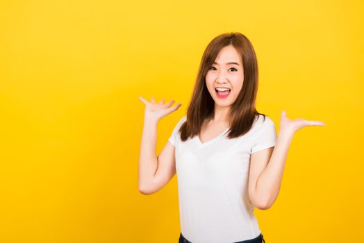 Asian happy portrait beautiful cute young woman teen standing wear t-shirt Surprised excited screaming open mouth show hand looking to camera isolated, studio shot on yellow background with copy space