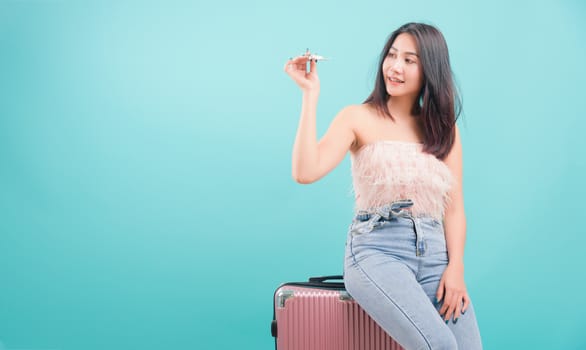 Asian happy portrait beautiful young woman standing smile in summer trip to travel, hat with a suitcase bag on blue background with copy space for text, Traveler tourist concept