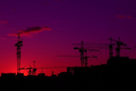 Construction cranes and houses black silhouette over sunset sky and clouds