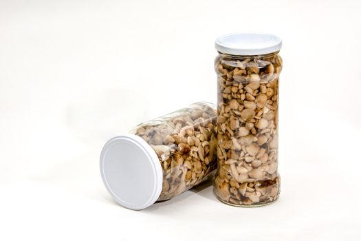 Marinated mushrooms in transparent, glass jars with white lids, isolated, against a white background