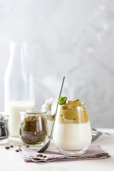 Glass with water drops of iced frothy drink Dalgona Coffee, trend korean drink latte espresso with coffee. White wooden table surface.