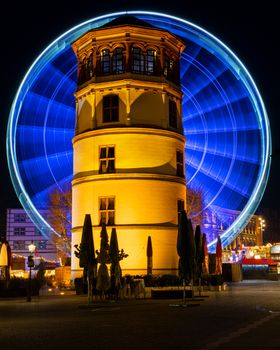 In motion - illuminated giant wheel behind the castle tower of Dusseldorf at night, Germany.