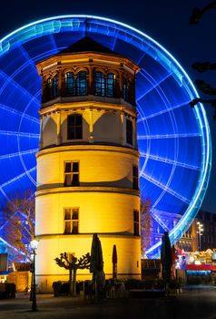 In motion - illuminated giant wheel behind the castle tower of Dusseldorf at night, Germany.