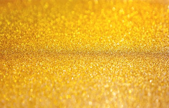 Golden abstract background with shiny glitter. Festive sparkling macro texture. Holiday backdrop with copy space.